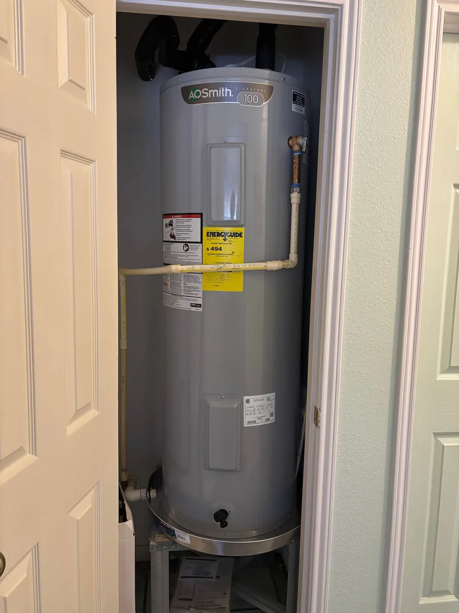 Tall AO Smith electric water heater on a drain pan inside a narrow interior closet