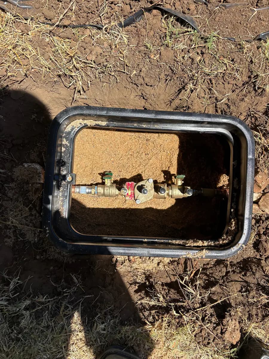 Brass backflow preventer assembly with green-handled shut-off valves set in an in-ground valve box
