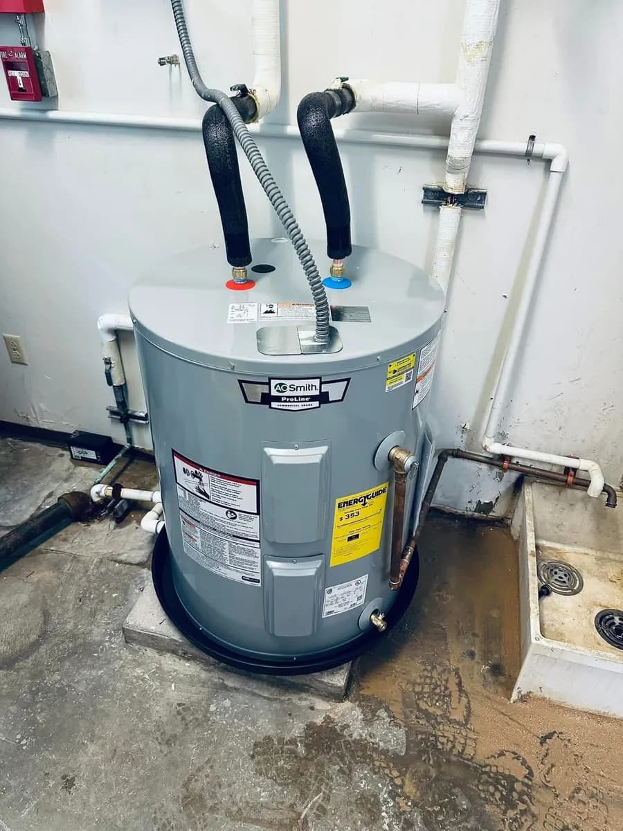 AO Smith ProLine commercial electric water heater on a drain pan in a mechanical room with flexible connectors