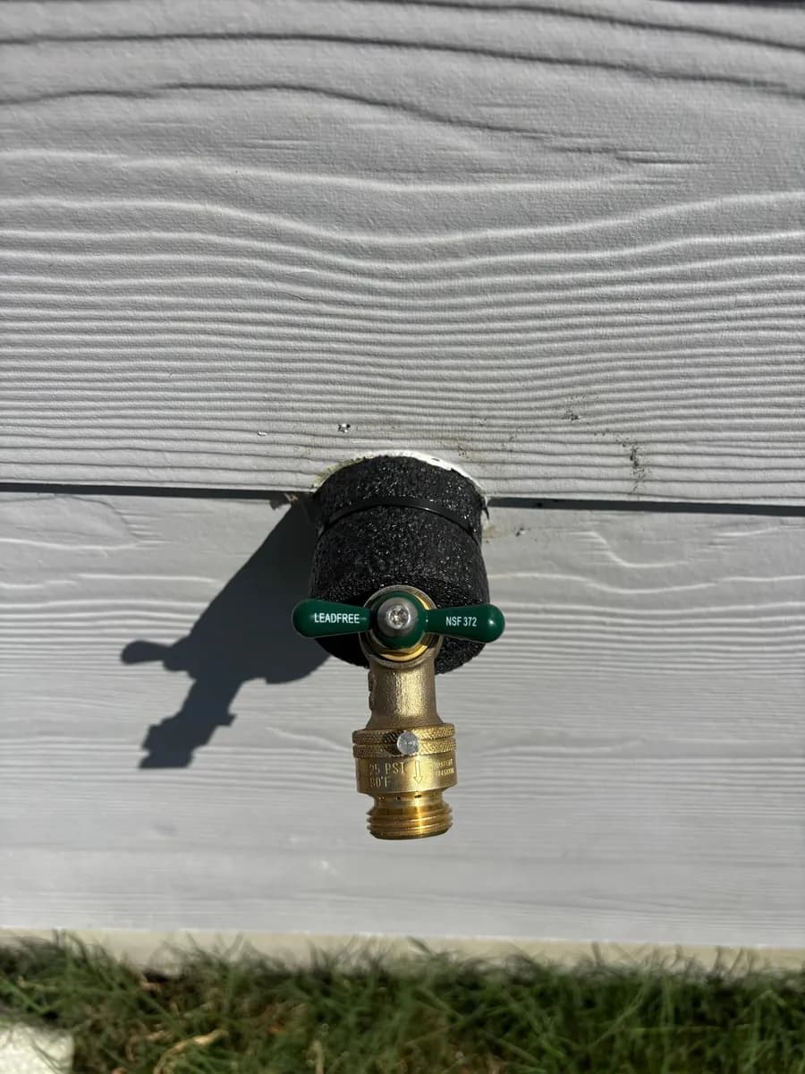 New lead-free brass hose bibb with a green handle installed through lap siding and sealed at the wall
