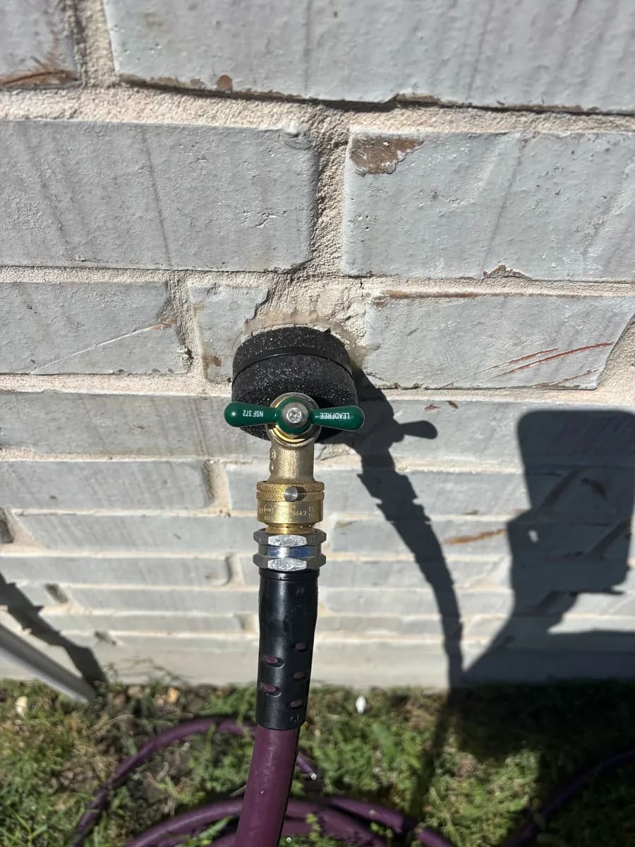Replacement brass hose bibb on a painted brick wall with a garden hose connected