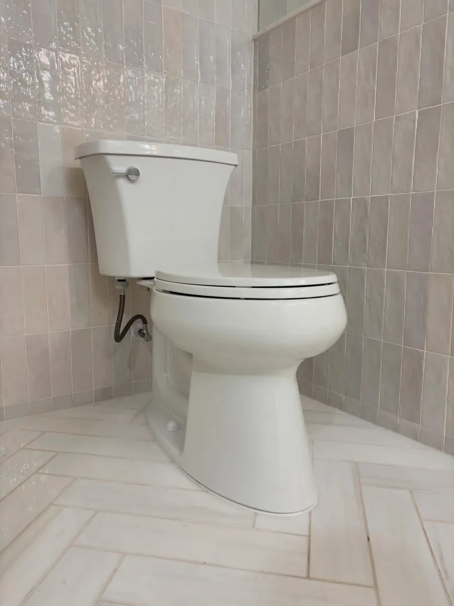 Newly set white two-piece toilet against tiled walls and herringbone tile flooring