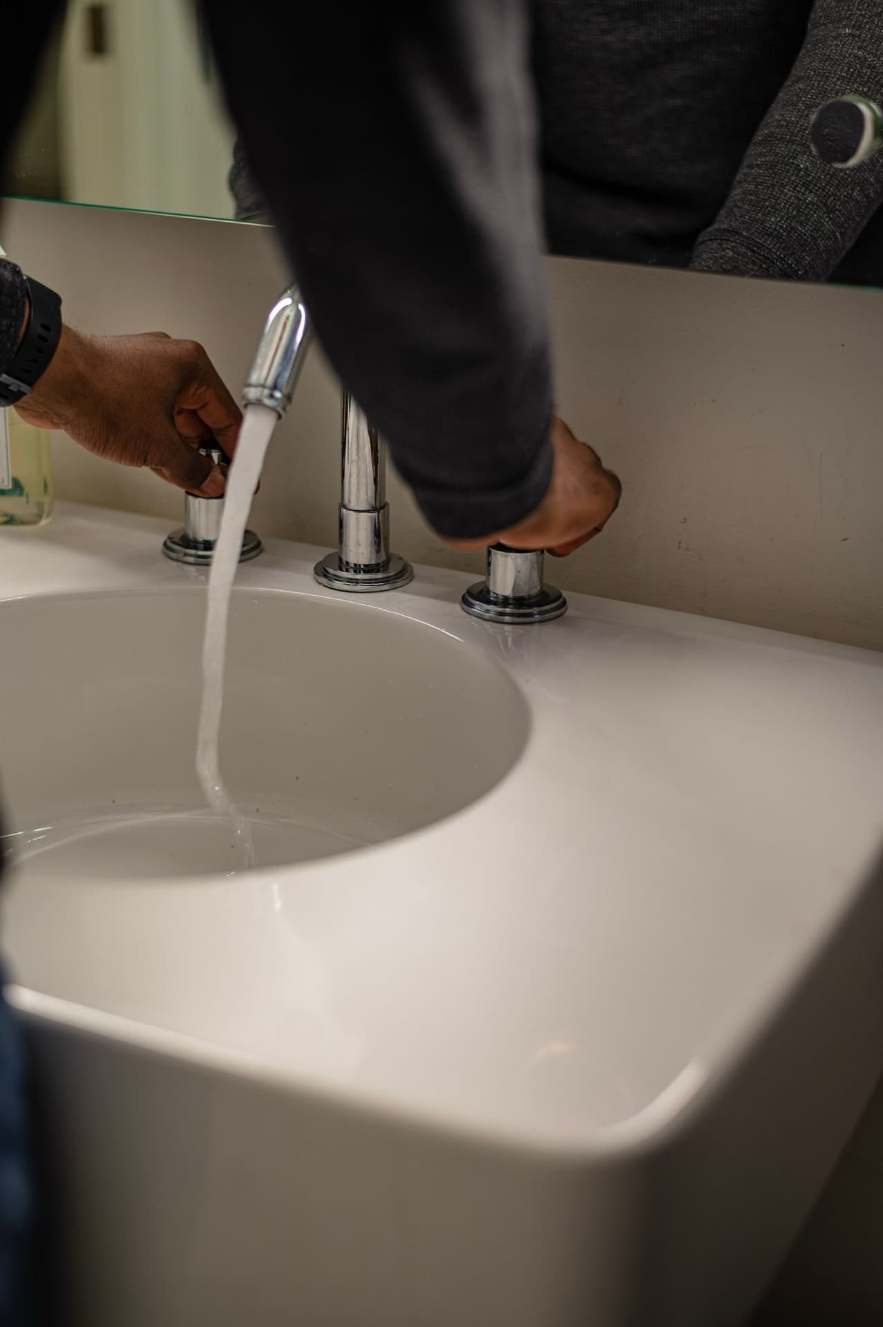 Hands adjusting faucet at a white sink with water running