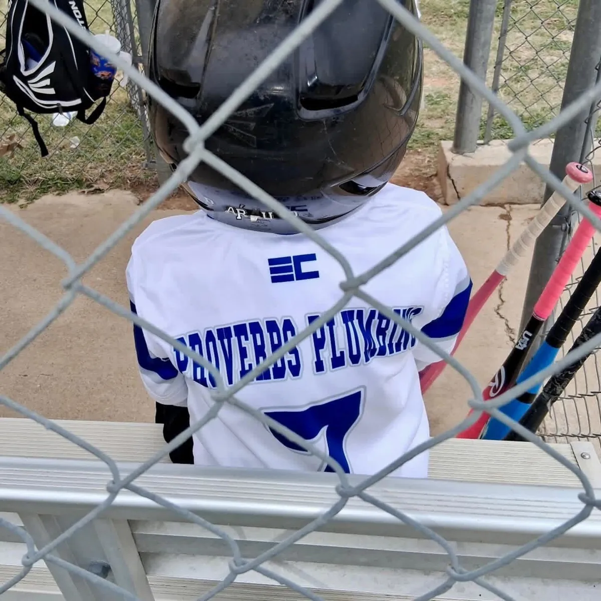 Young ballplayer in a Proverbs Plumbing sponsored team jersey waiting in the dugout