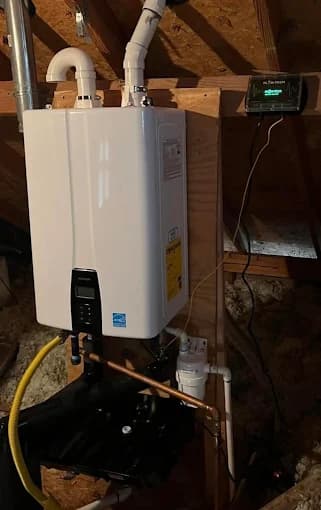 Wall-mounted tankless water heater installed in an attic with a digital monitoring panel